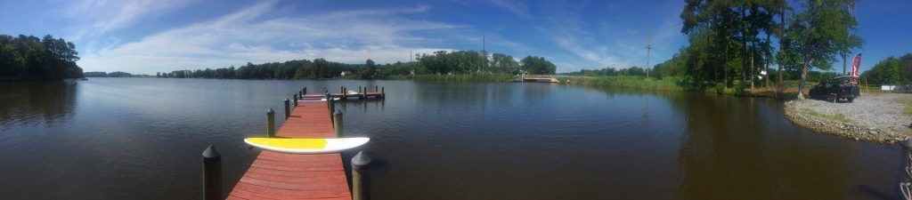 Dock on a river in a forest with a white yellow paddle board in the middle of the walkway.